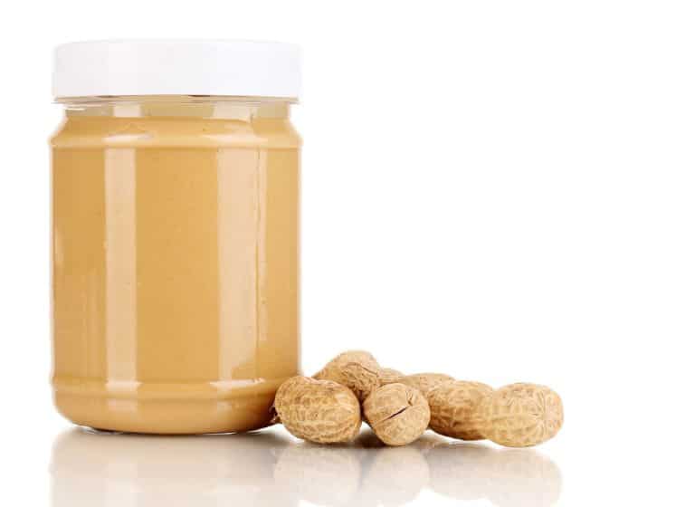 A jar of peanut butter next to some peanuts.