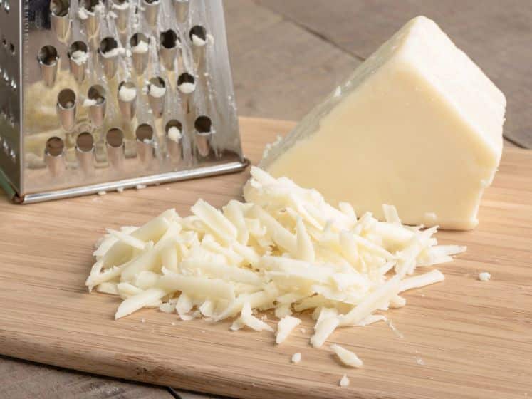 Fresh parmesan cheese with a metal grated on a cutting board