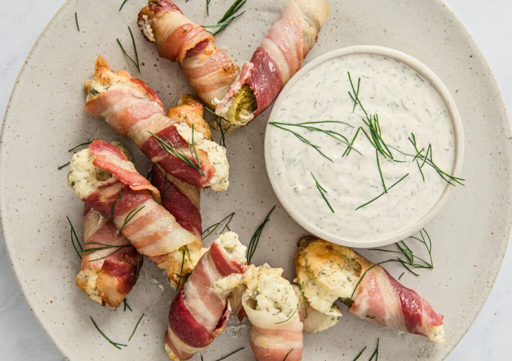 Bacon pickle boats with dip on a plate garnished with fresh dill.