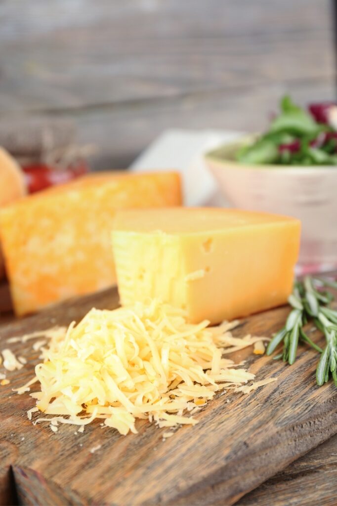 Grated cheddar cheese and a block of cheese on a wooden cutting board.