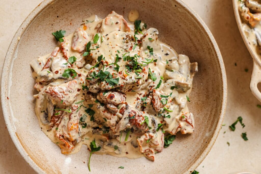 Chicken with creamy mushroom sauce in a bowl garnished with herbs.