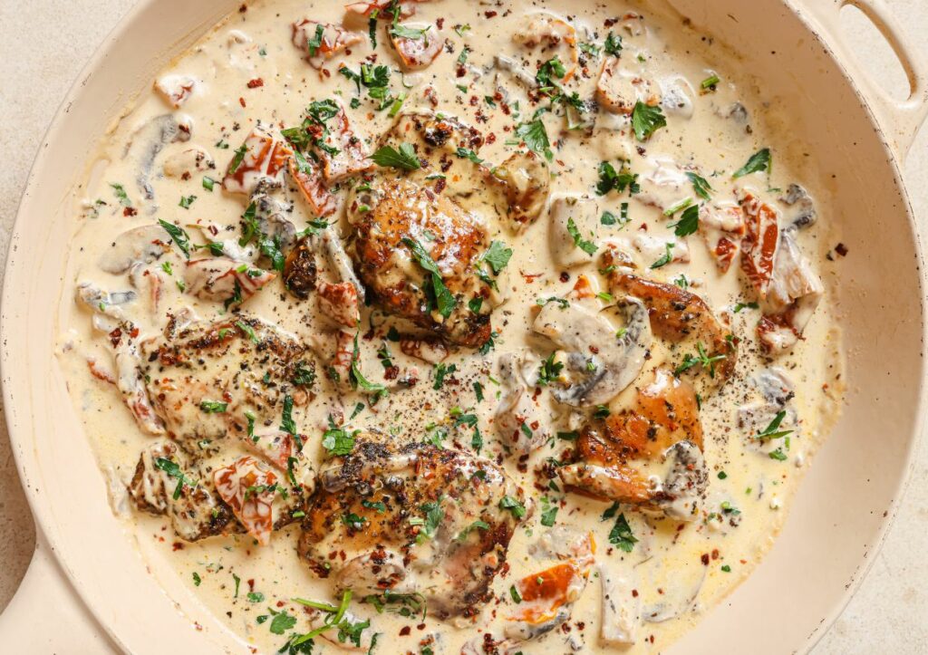 Chicken with creamy mushroom sauce in a skillet garnished with fresh herbs.