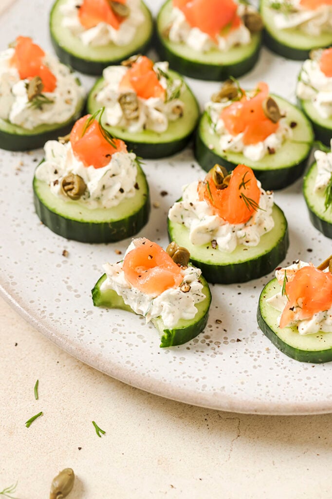 Garnished cucumber and dill smoked salmon appetizer on a plate, with one piece bitten.