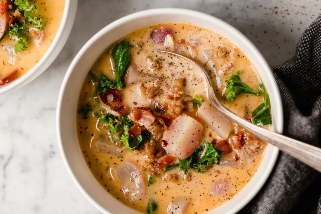 Keto zuppa Toscana in a bowl with a spoon on a marble countertop.