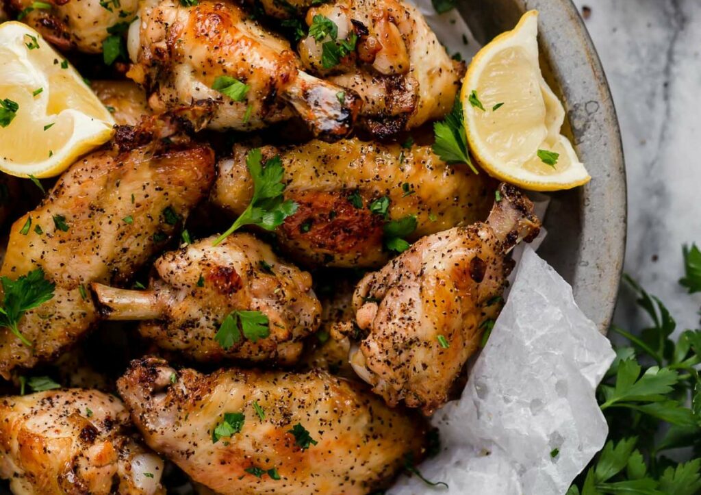 Lemon pepper chicken wings in a serving dish with lemon wedges and parsley.