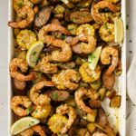 Garnished sheet pan shrimp boil on a sheet pan with a wooden spoon.