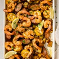 Garnished sheet pan shrimp boil on a sheet pan with a wooden spoon.