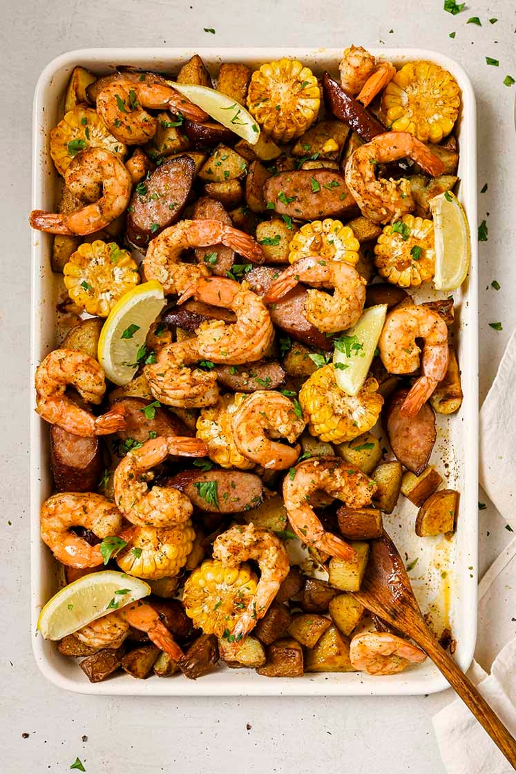 Garnished sheet pan shrimp boil on a sheet pan with a wooden spoon.