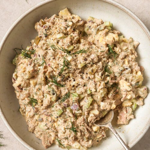 Tuna egg salad garnished with dill and freshly-cracked black pepper on a plate with a spoon.