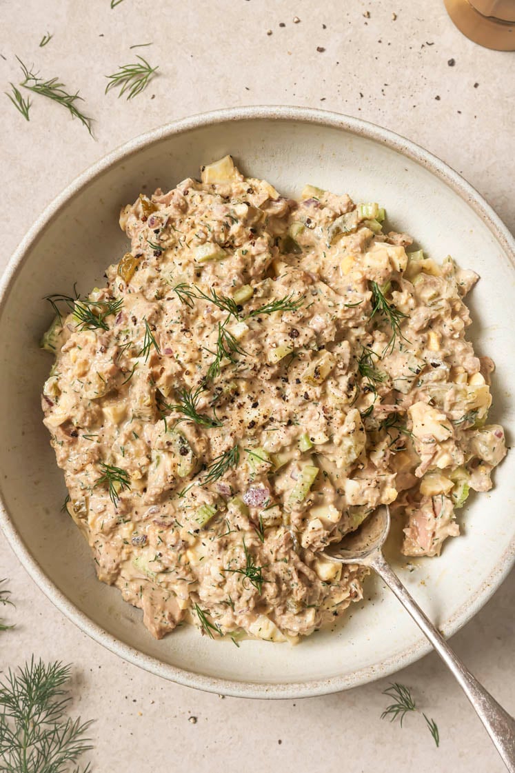 Tuna egg salad garnished with dill and freshly-cracked black pepper on a plate with a spoon.