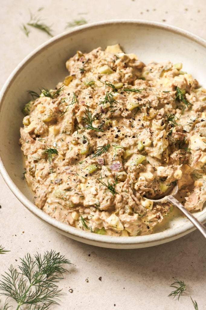 Tuna egg salad garnished with dill and freshly-cracked black pepper on a plate with a spoon.