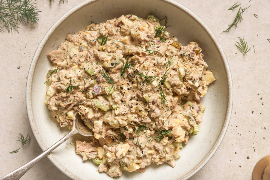 Tuna egg salad garnished with dill and freshly-cracked black pepper on a plate with a spoon.