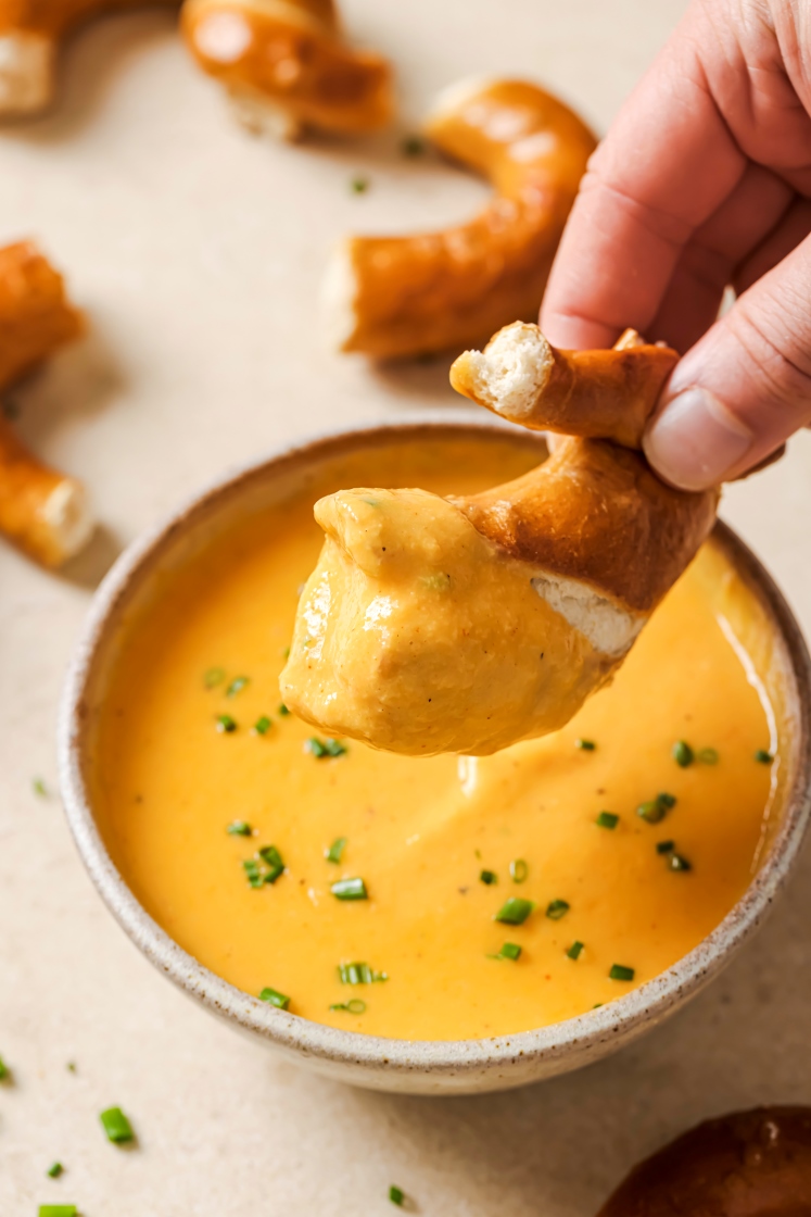 A hand holding a soft pretzel piece after dunking it in beer cheese dip.