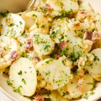 Garnished German potato salad in a bowl with a spoon.