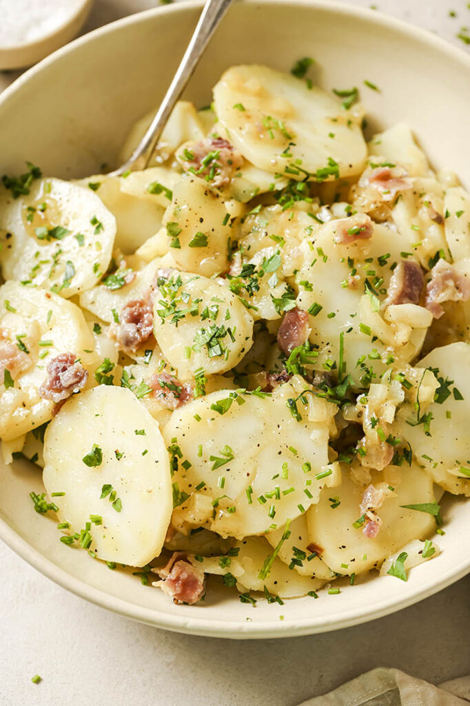 Garnished German potato salad in a bowl with a spoon.