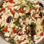 Garnished Italian orzo pasta salad in a bowl with a spoon.