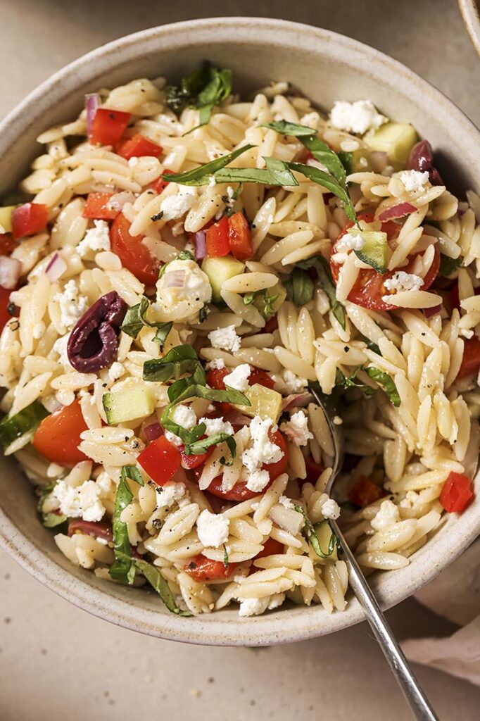 Garnished Italian orzo pasta salad in a bowl with a spoon.