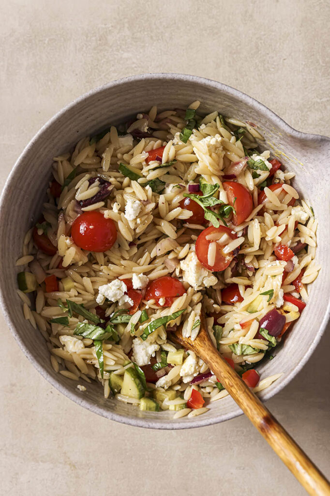 Garnished Italian orzo pasta salad in a bowl with a wooden spoon.