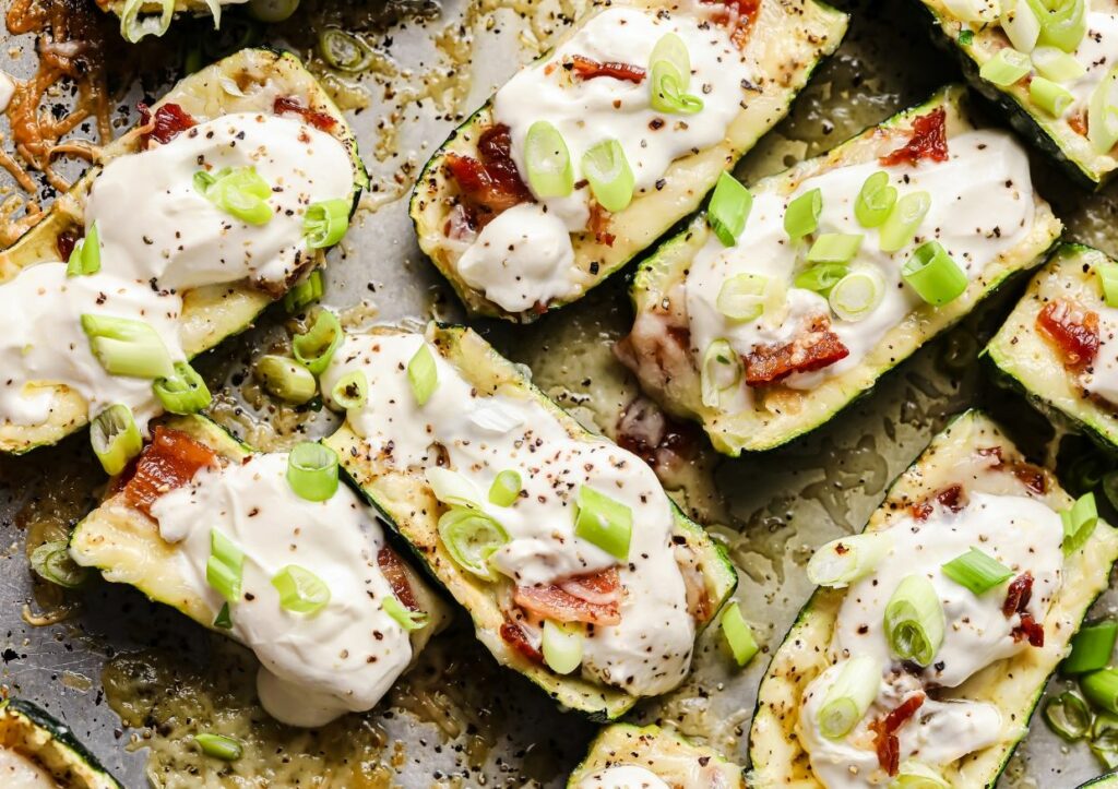 Loaded zucchini boats garnished with sour cream and green onions on a sheet pan.