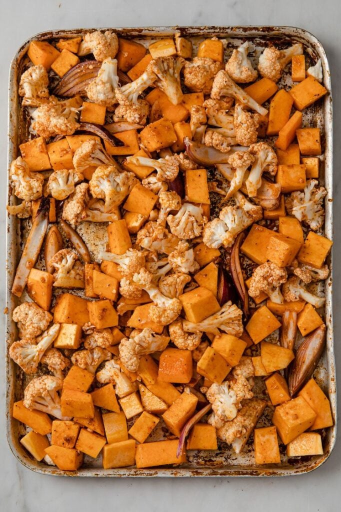 A baking sheet filled with cauliflower florets, cubed butternut squash, and sliced red onions.