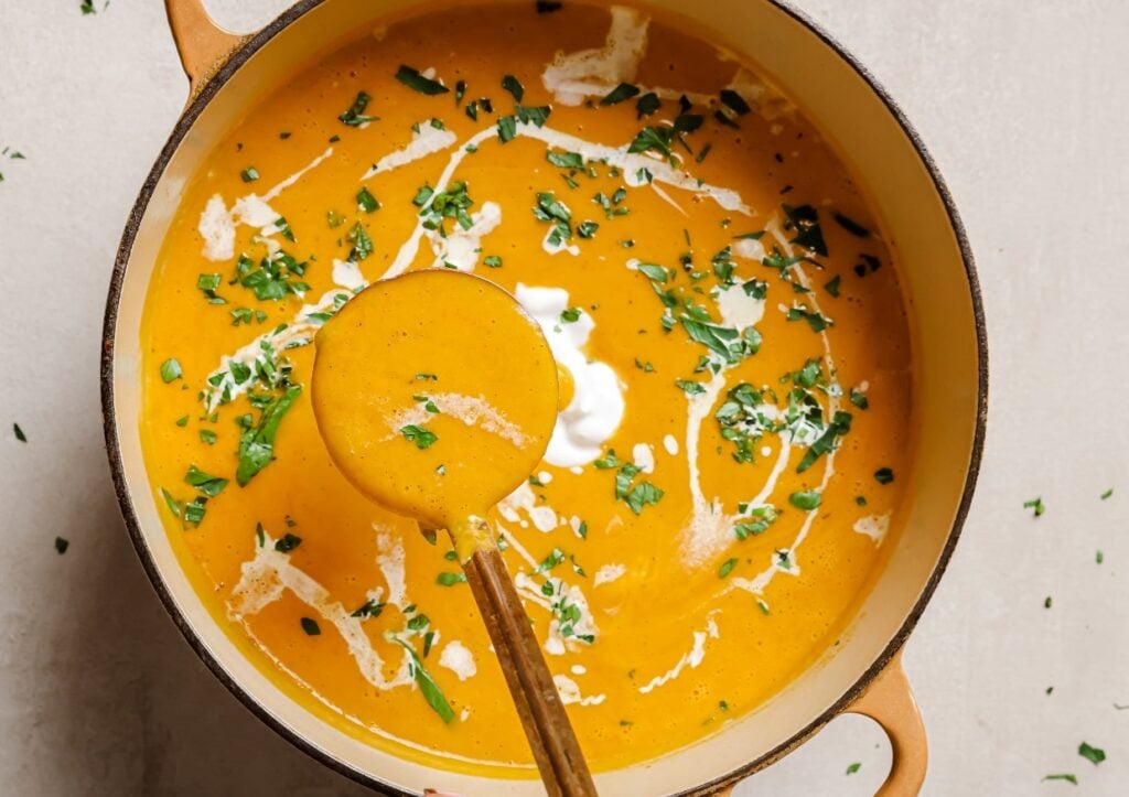 Sweet potato and red pepper soup with a ladle.