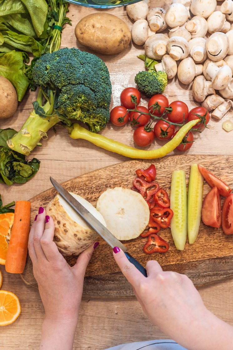 A person cutting fresh turnip on a wooden cutting board, with assorted veggies on the table.