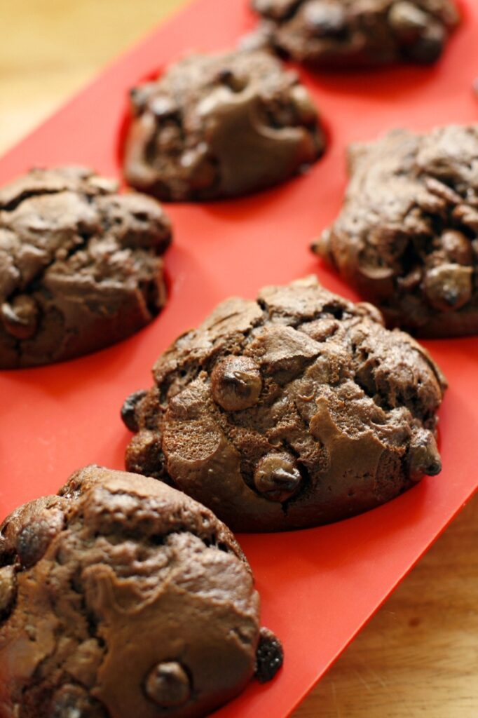 Close-up of freshly baked double chocolate chip cookies on a red silicone muffin pan.