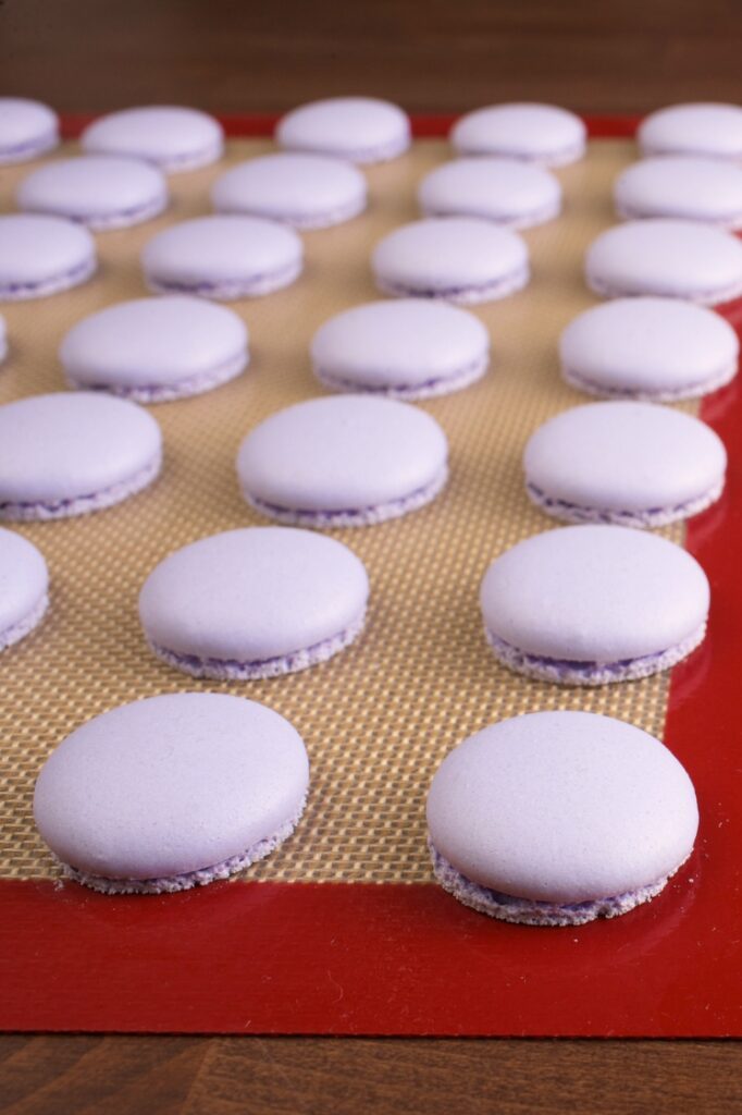 Baked purple macarons laid out on a silicone baking mat with a red border.