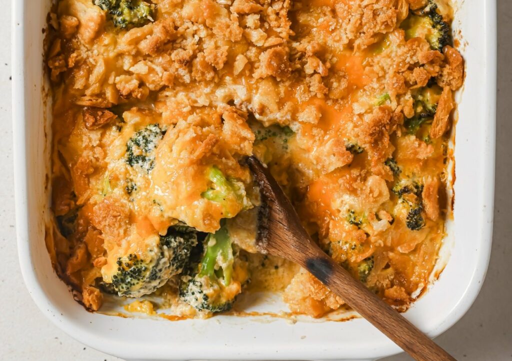 Broccoli casserole being served with a wooden spoon.