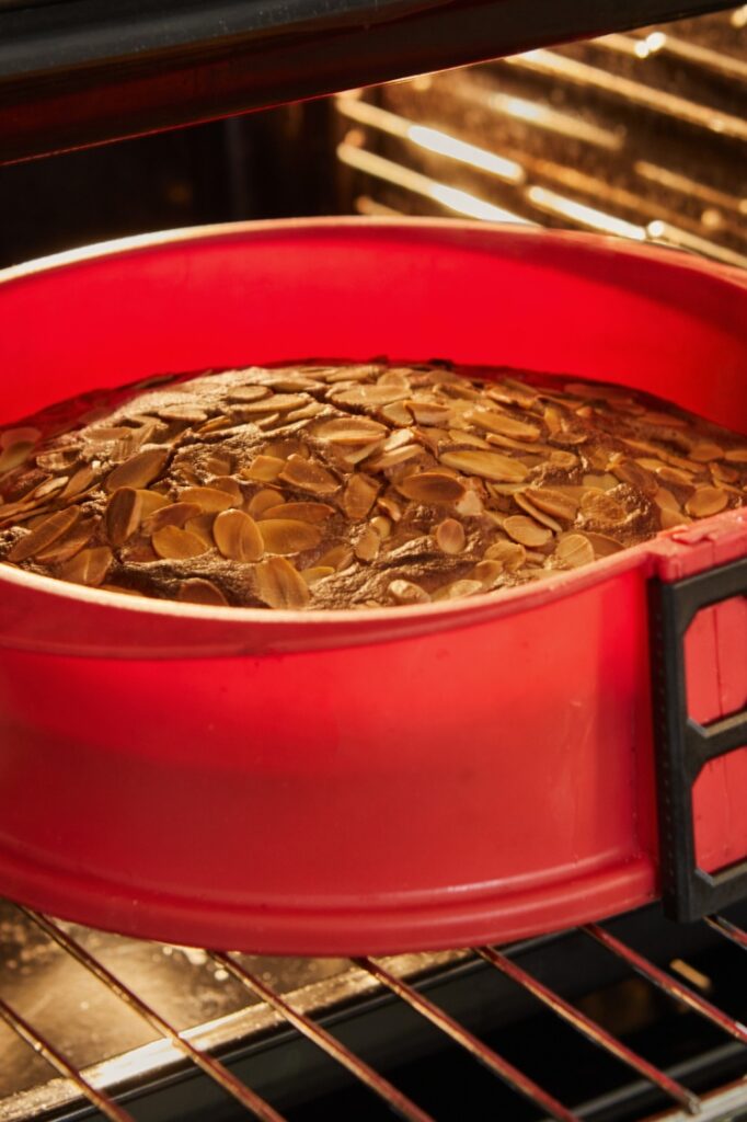 Chocolate almond cake baking in a red silicone cake pan in an oven.