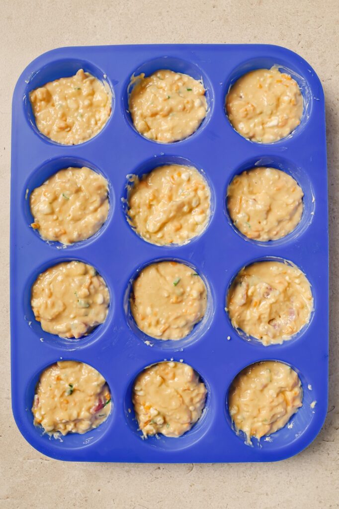 A blue silicone muffin tray filled with cottage cheese breakfast muffin batter.