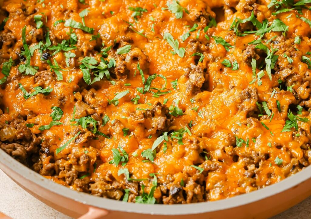 A pan of creamy ground beef skillet with cauliflower rice garnished with fresh herbs.