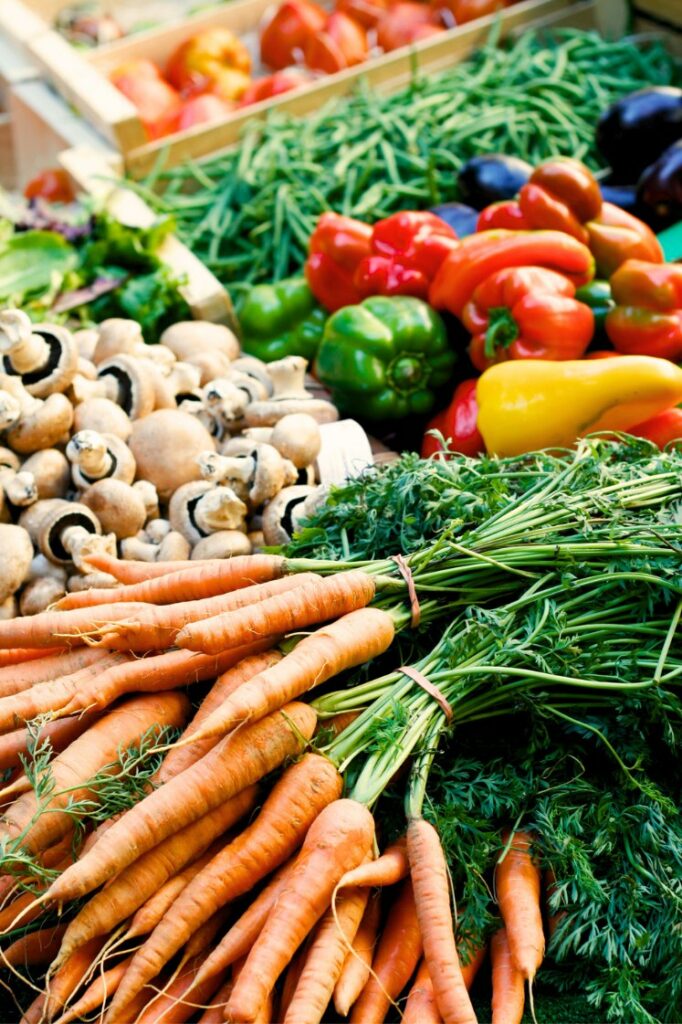 Fresh vegetables including carrots, peppers, and mushrooms on display at a farmer's market.