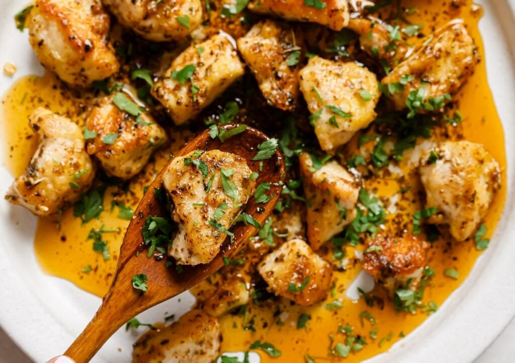 Garlic butter chicken bites on a plate with one chicken bite on a spoon.