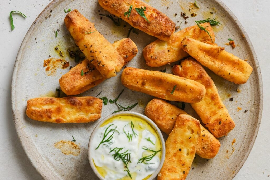 A plate of halloumi fries next to dipping sauce.