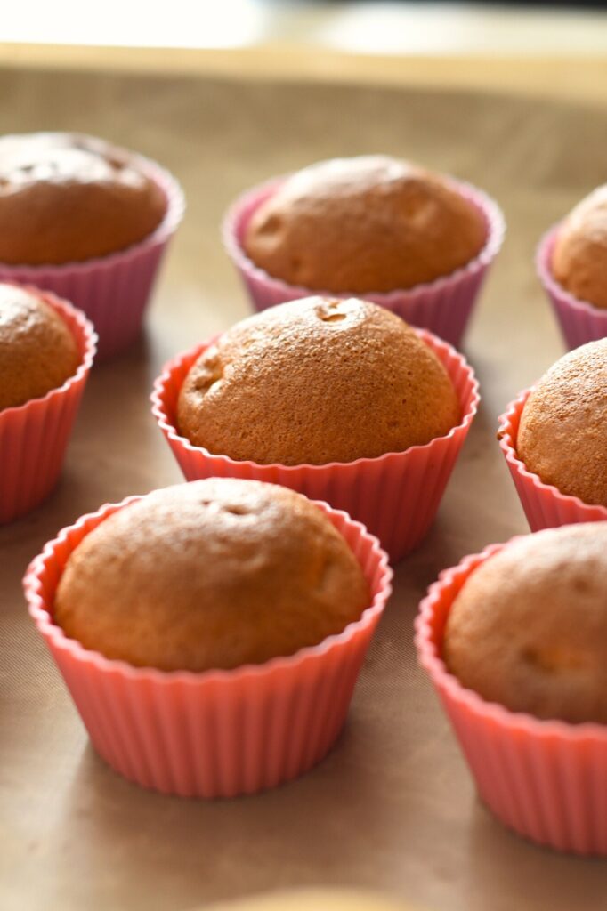 Freshly baked, mini-muffins placed in pink and purple silicone cups on a baking tray.