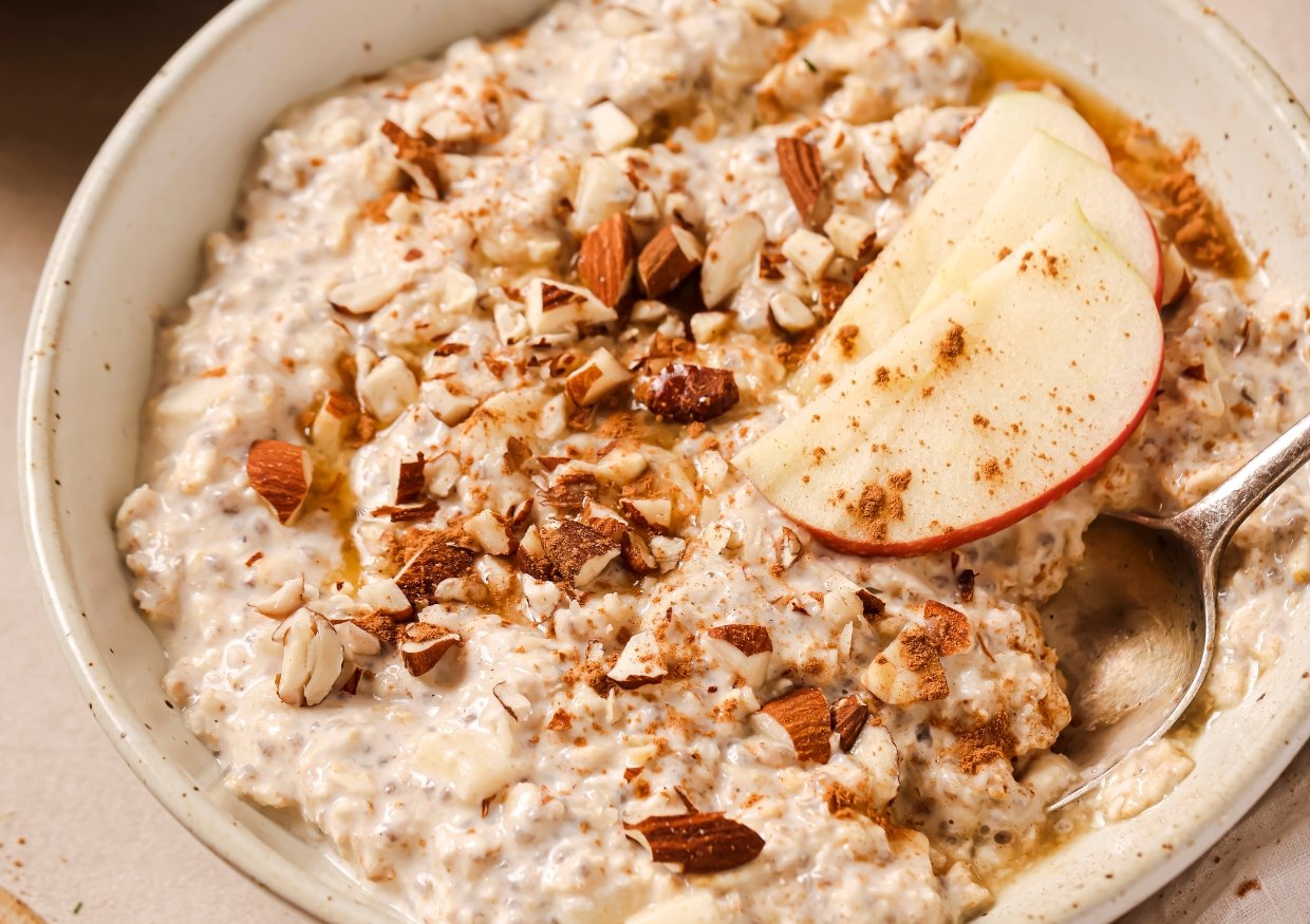 A bowl of chia seed pudding topped with chopped almonds, apple slices, and a drizzle of honey. A spoon is placed in the pudding.