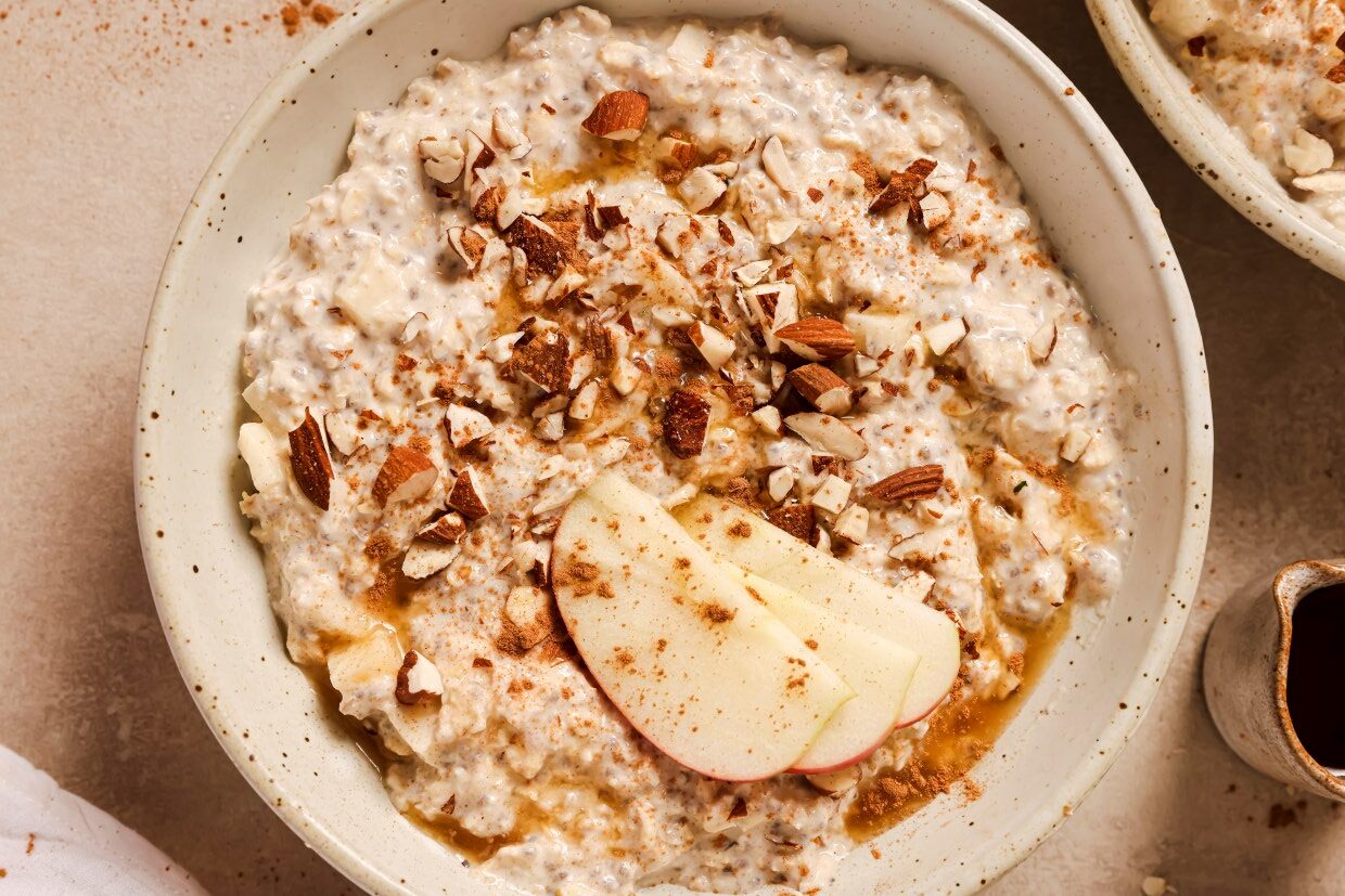 A bowl of oatmeal topped with chopped nuts, apple slices, and a sprinkle of cinnamon.