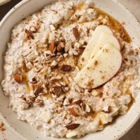 A bowl of overnight apple pie oats garnished with chopped almonds, apple slices, cinnamon and maple syrup.