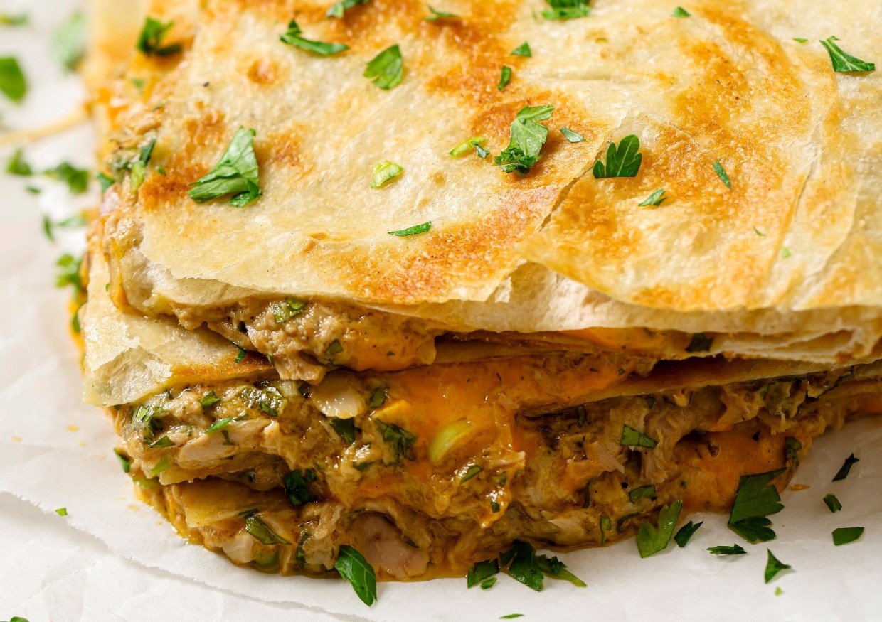 Close-up of a quesadilla featuring melted cheese and chopped herbs, garnished with fresh parsley.