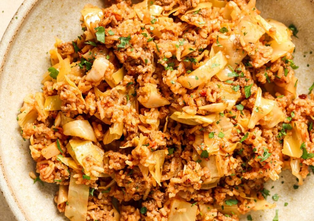 A plate of stir-fried rice with shredded cabbage, pieces of meat, and garnished with chopped herbs.