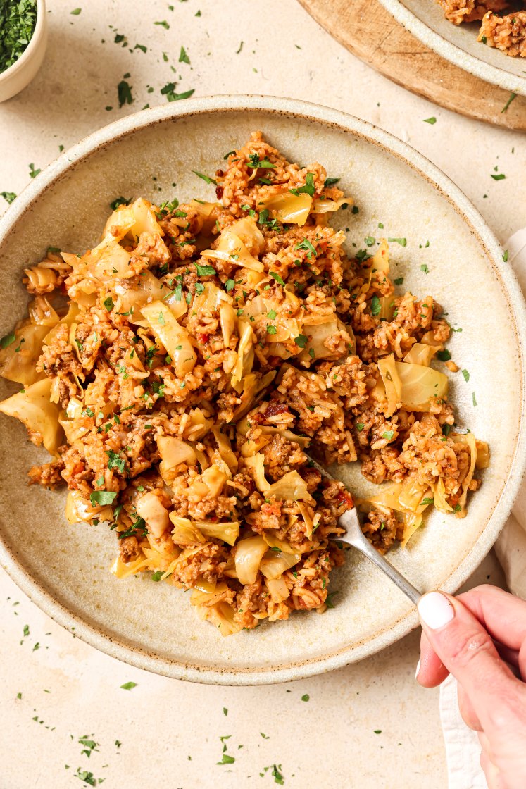 A hand holding a fork of unstuffed cabbage rolls on a plate.