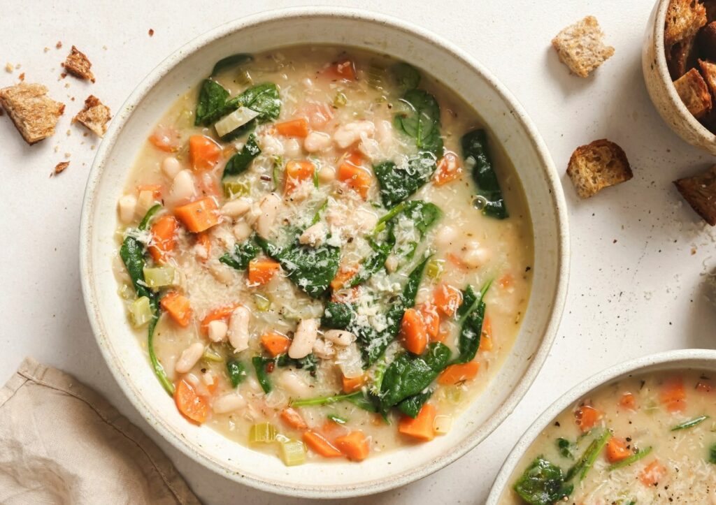 White bean soup in a bowl with croutons surrounding it.