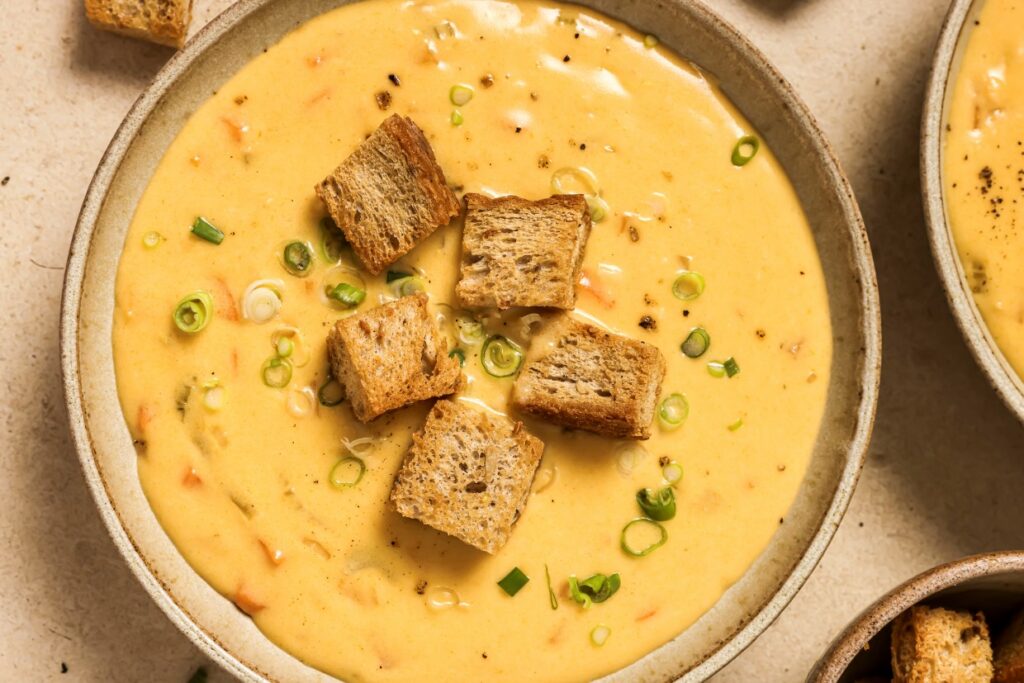 A bowl of creamy soup topped with croutons and chopped green onions.