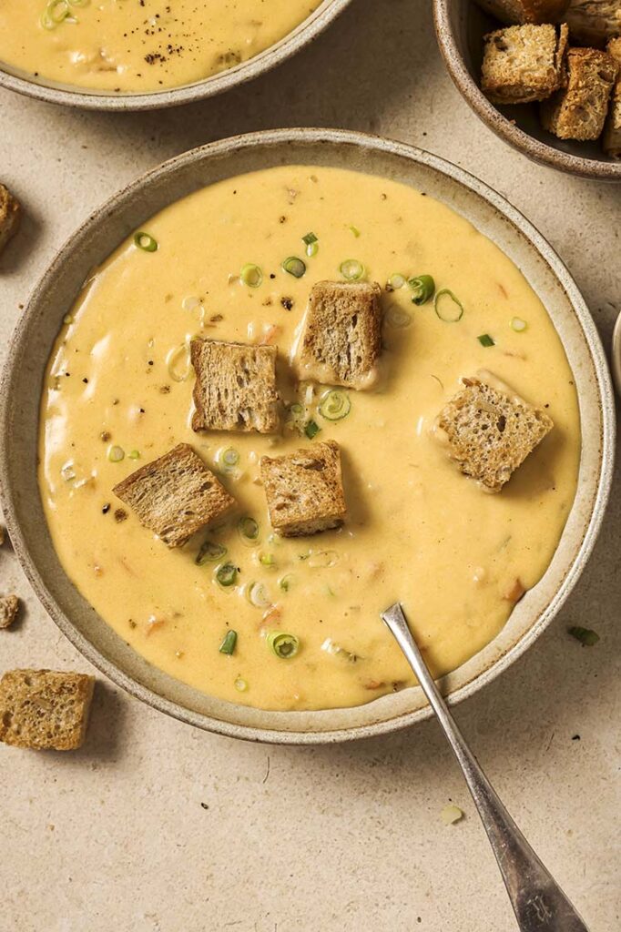 A bowl of Wisconsin beer cheese soup with croutons and chives with a spoon.