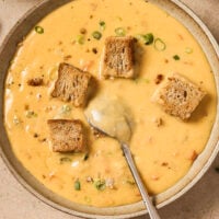 A bowl of Wisconsin beer cheese soup with croutons and chives with a spoon.