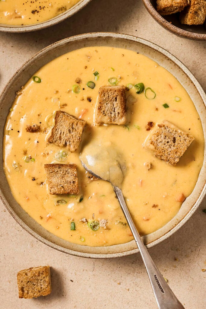 A bowl of Wisconsin beer cheese soup with croutons and chives with a spoon.