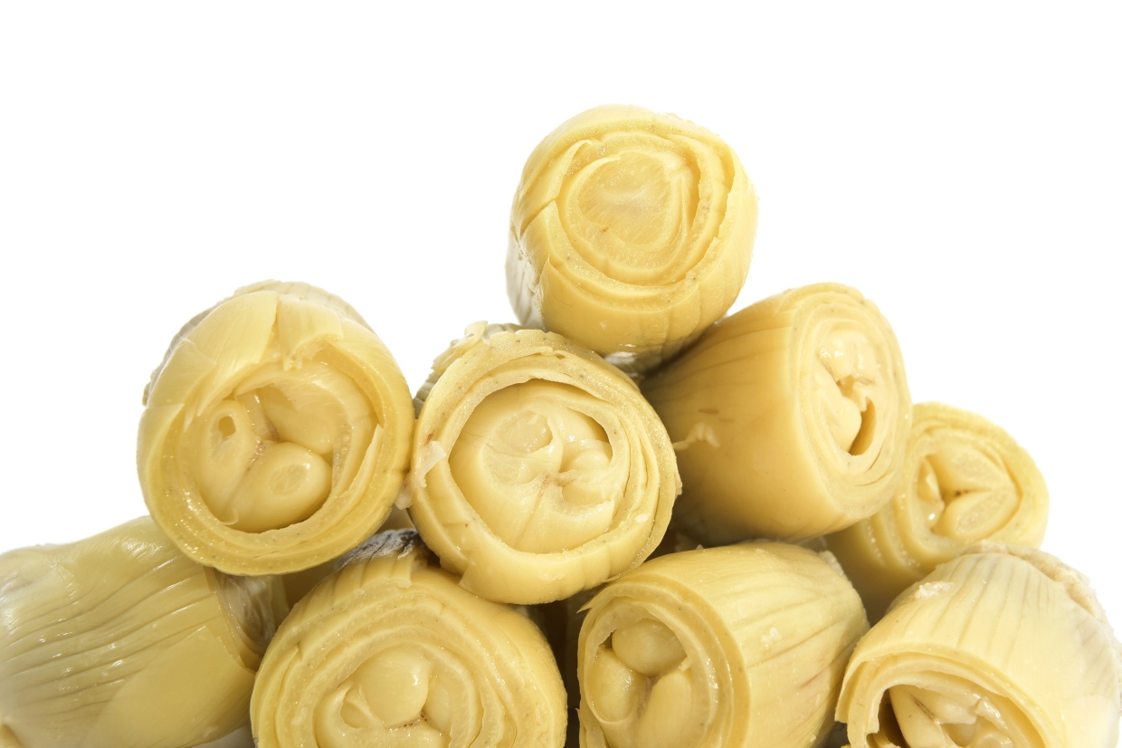 Close-up of several artichoke hearts arranged in a pyramid shape against a white background. The artichokes appear fresh and moist, showcasing their layered texture and pale yellow color.