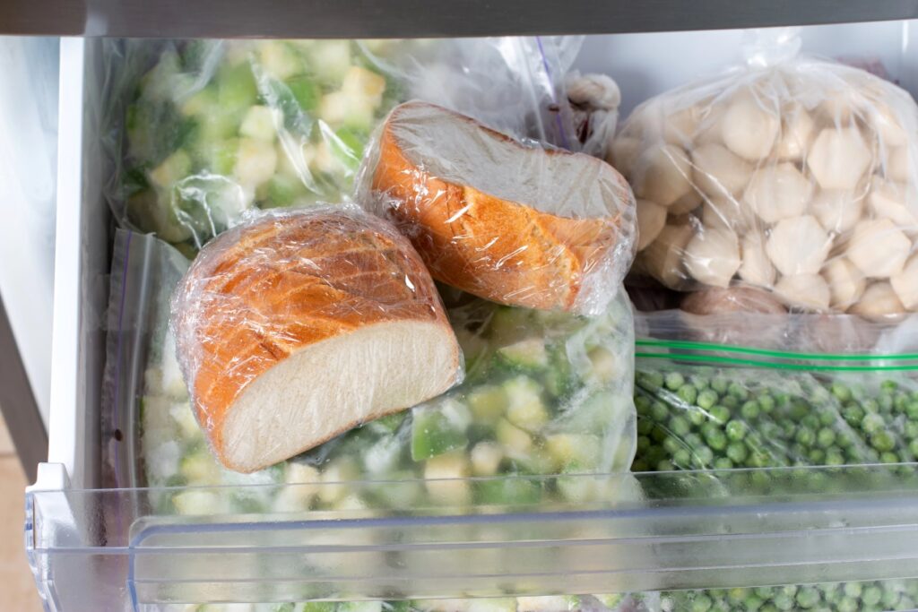 Sliced bread wrapped in plastic in a freezer along with other frozen food.