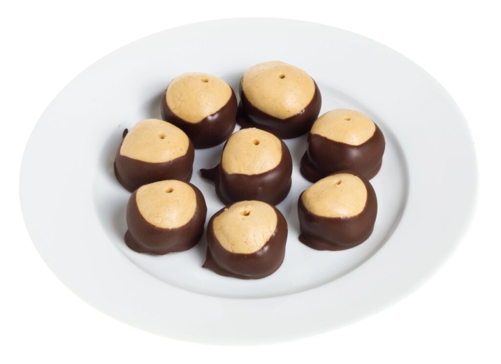 A white plate with eight buckeye candies, featuring creamy peanut butter centers partially dipped in dark chocolate.